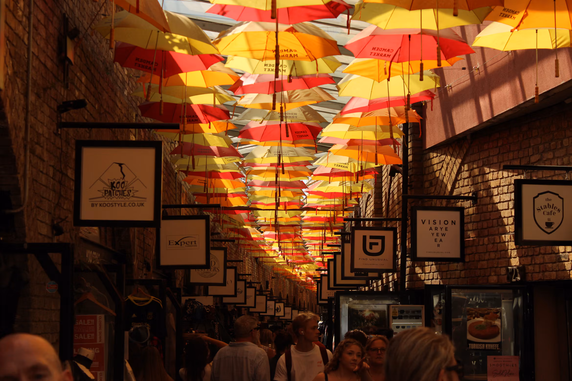 Colourful umbrellas suspended above a busy covered shopping passage in Camden Market
