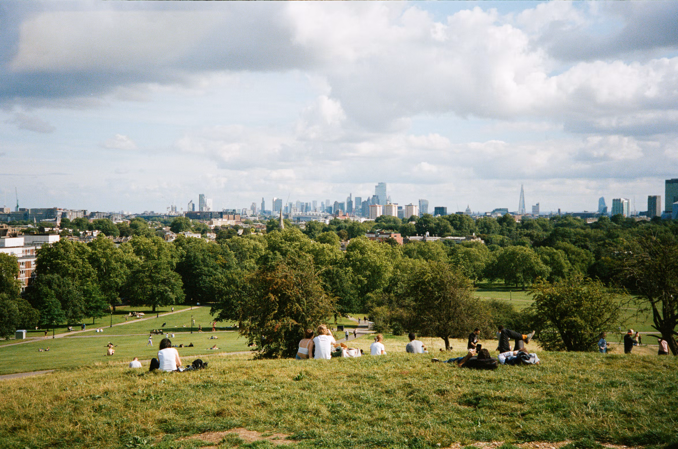 People relaxing on the grass at Primrose Hill with the London skyline beyond